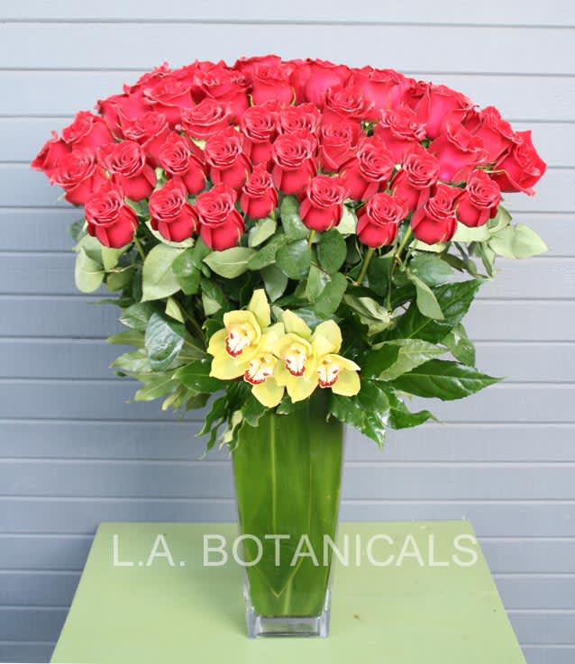Tall bouquet of red roses with yellow orchids in a glass vase
