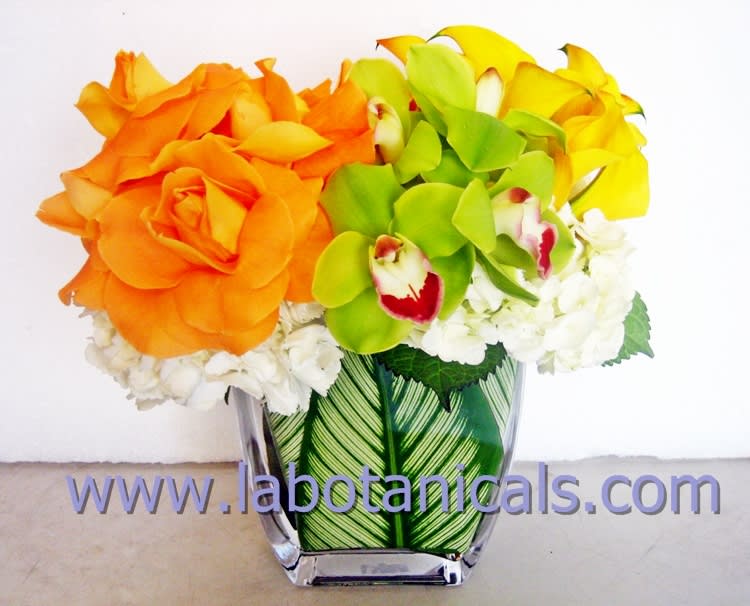 Orange roses, green orchids, and yellow blooms in a clear vase