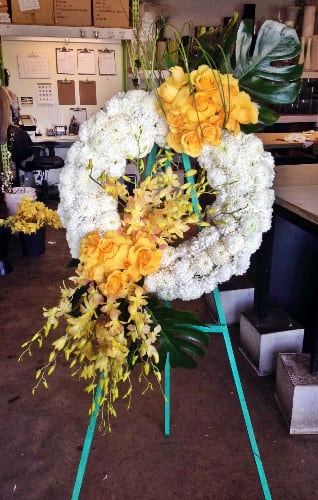 Large floral wreath with yellow roses and white blooms on a stand