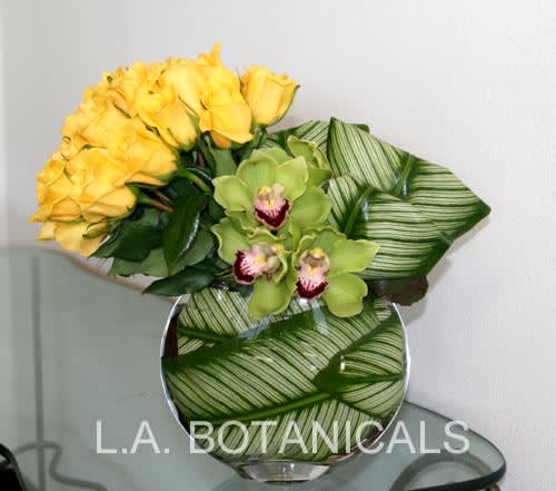 Yellow roses and green orchids in a round glass vase