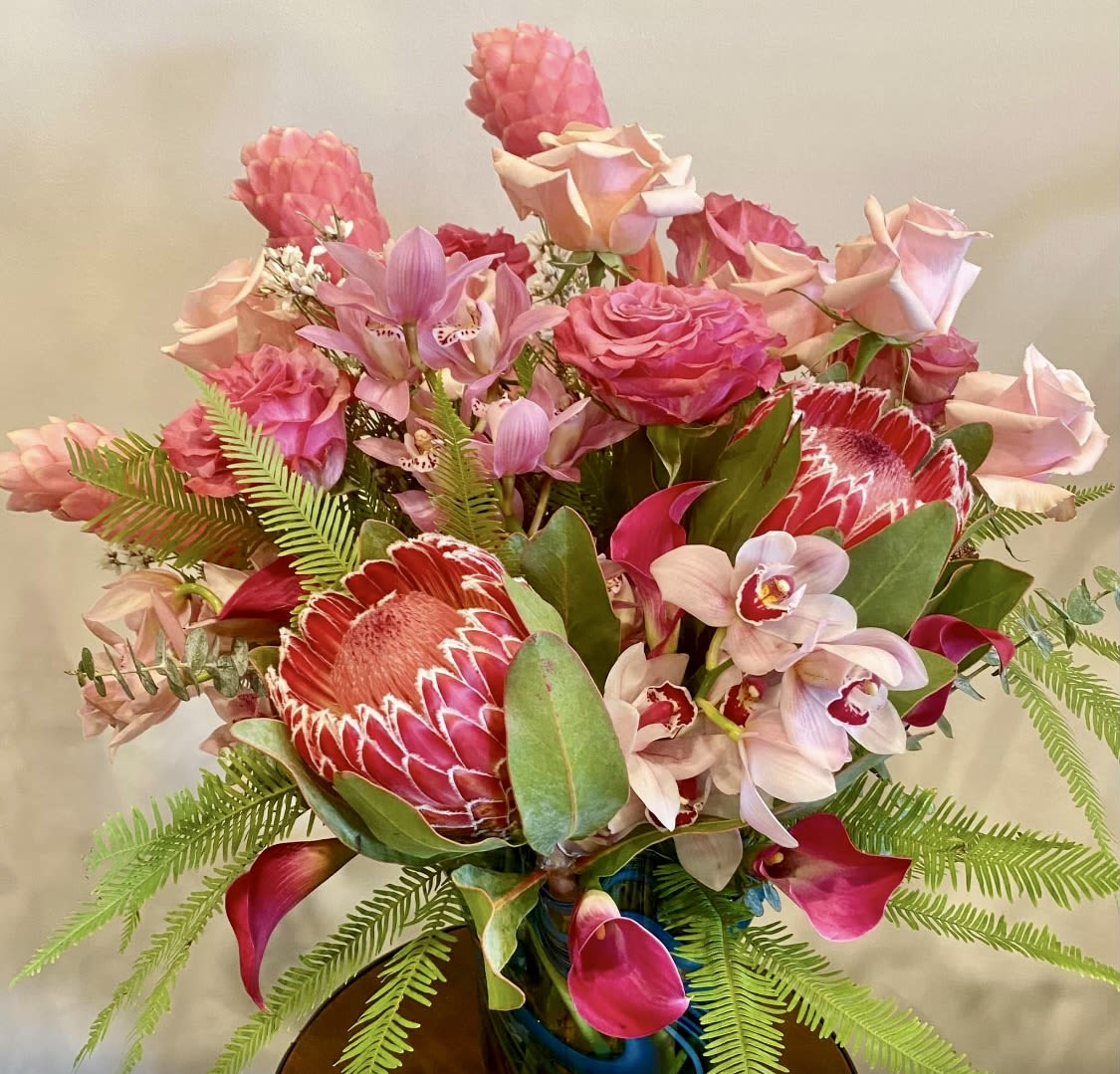 Pink and red tropical bouquet with roses, orchids, and protea in a vase