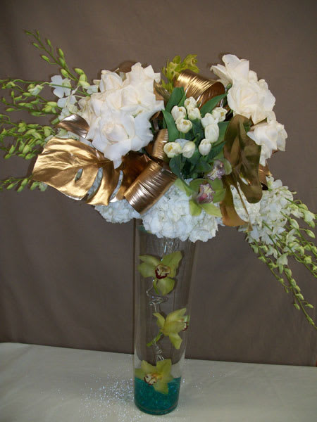 White floral arrangement in a tall glass vase with gold ribbon accents