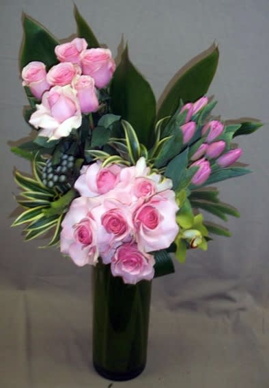 Pink roses arranged in a tall dark vase with broad green leaves.