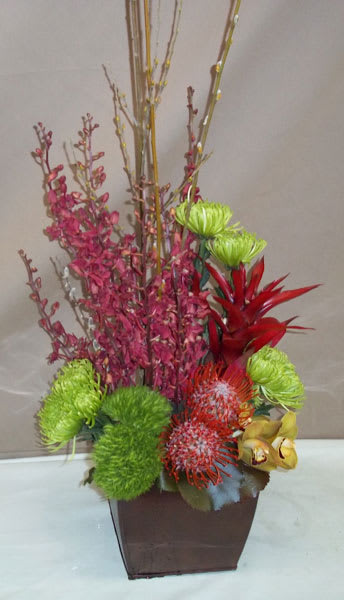 Tall floral arrangement in a brown square container with bright green, red, and pink blooms