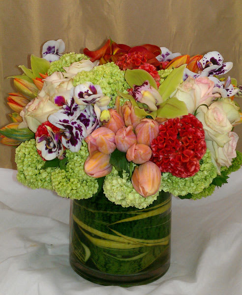 Mixed bouquet in a glass vase with orchids, roses, tulips, and green hydrangeas