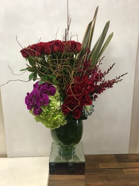 Tall bouquet of red roses, purple orchids, and green hydrangeas in a glass vase