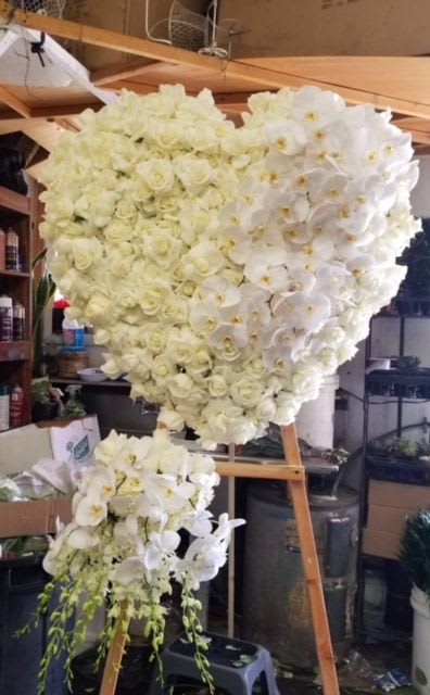Heart-shaped floral arrangement of white roses and orchids on an easel