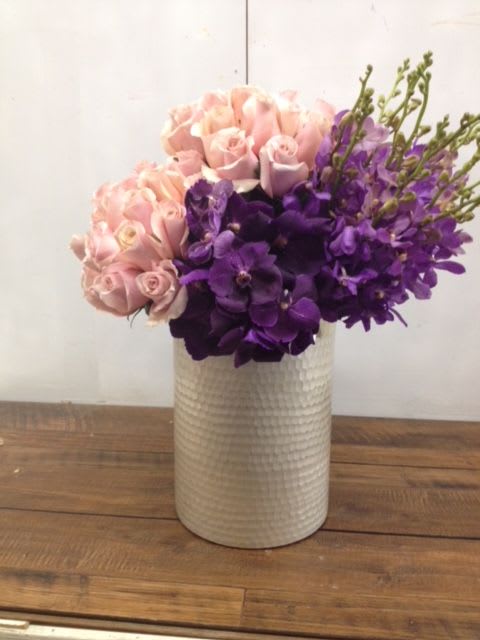 Pink roses and purple orchids arranged in a white vase