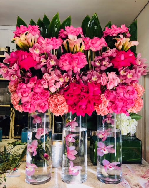 Pink floral arrangements in tall glass cylinders with orchids and roses