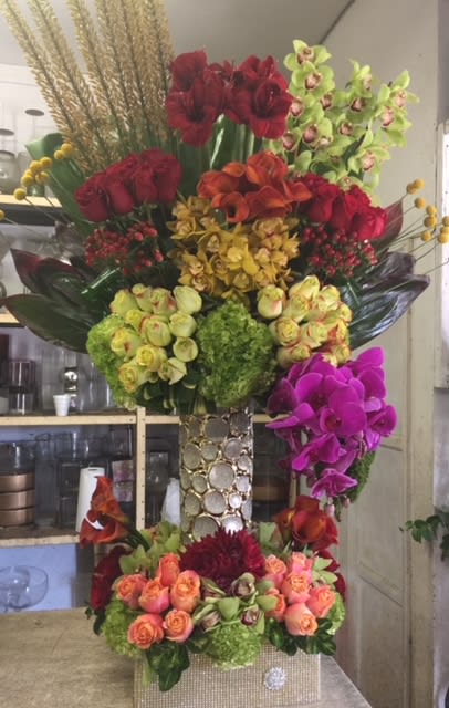 Tall floral arrangement with red, orange, yellow, green, and purple blooms in a decorative vase.