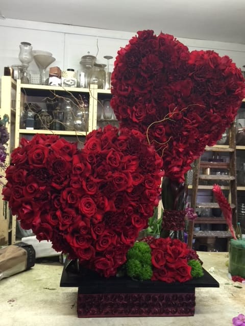 Two large heart-shaped red rose arrangements on a black base