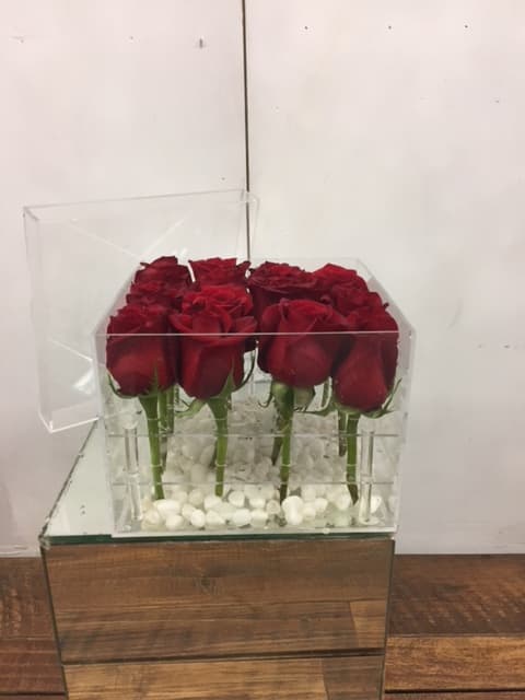 Red roses arranged in a clear acrylic box with white stones