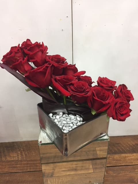 Red roses arranged in a square mirrored vase with silver stones