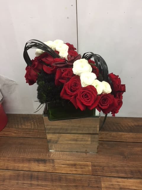 Red and white roses arranged in a square glass vase with black handles