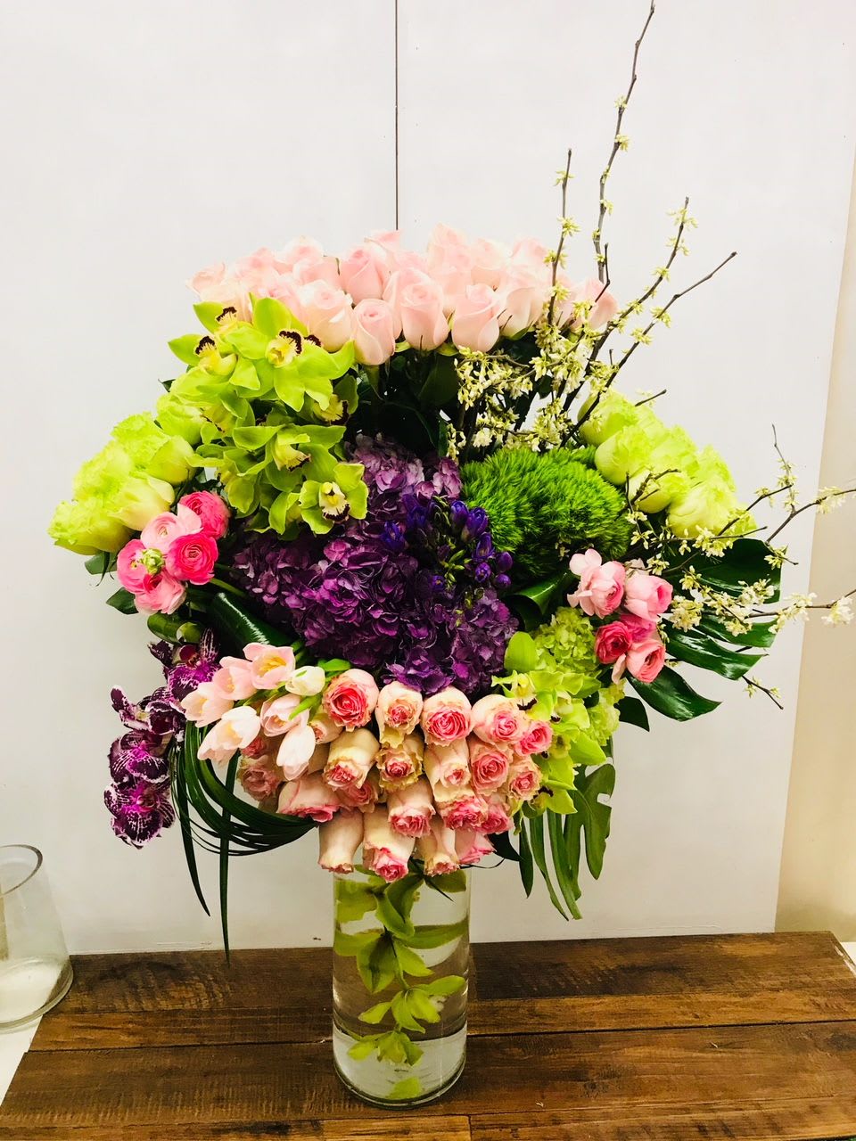 Large mixed bouquet in a clear glass vase with pink, green, and purple flowers