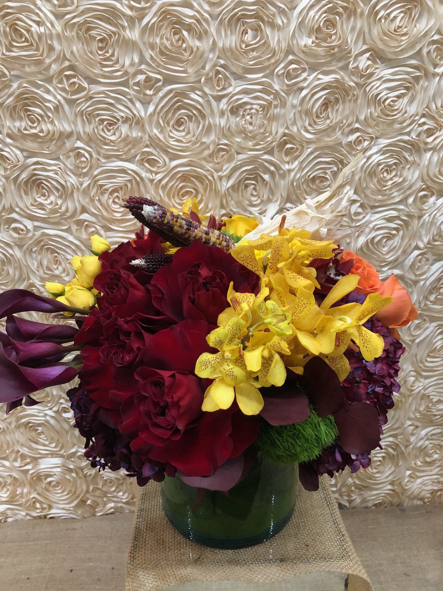 Bouquet of red roses, yellow orchids, and purple calla lilies in a glass vase