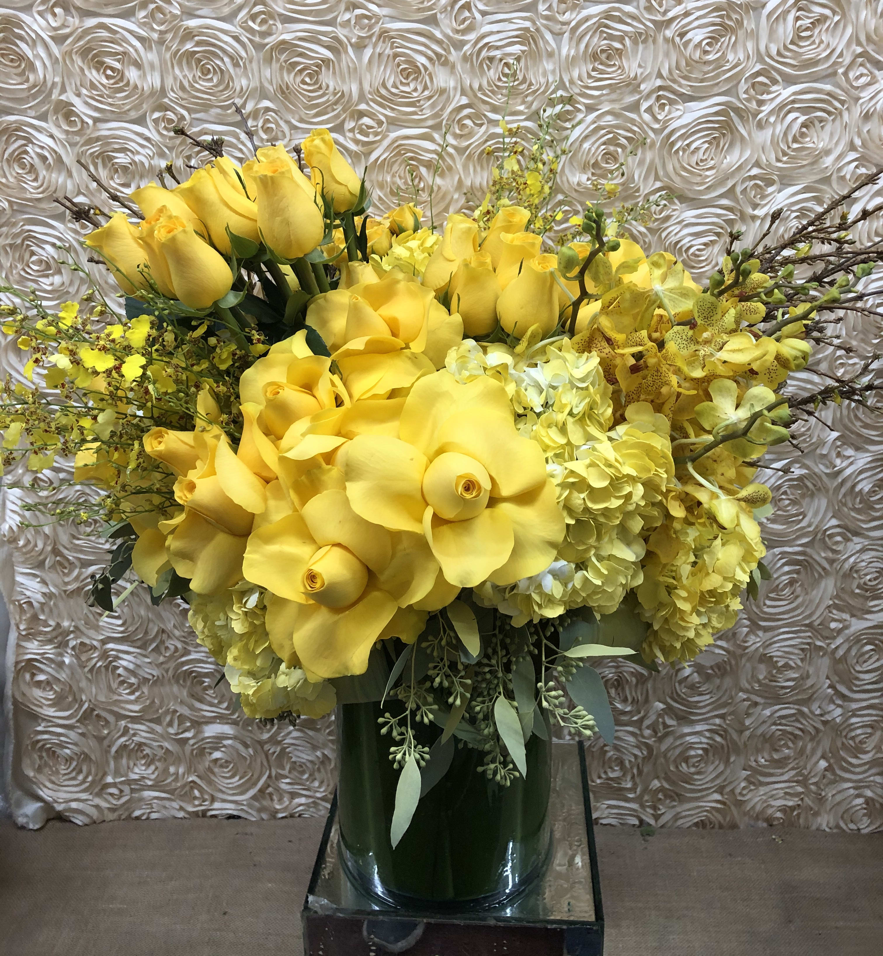 Yellow floral arrangement with roses and orchids in a glass vase