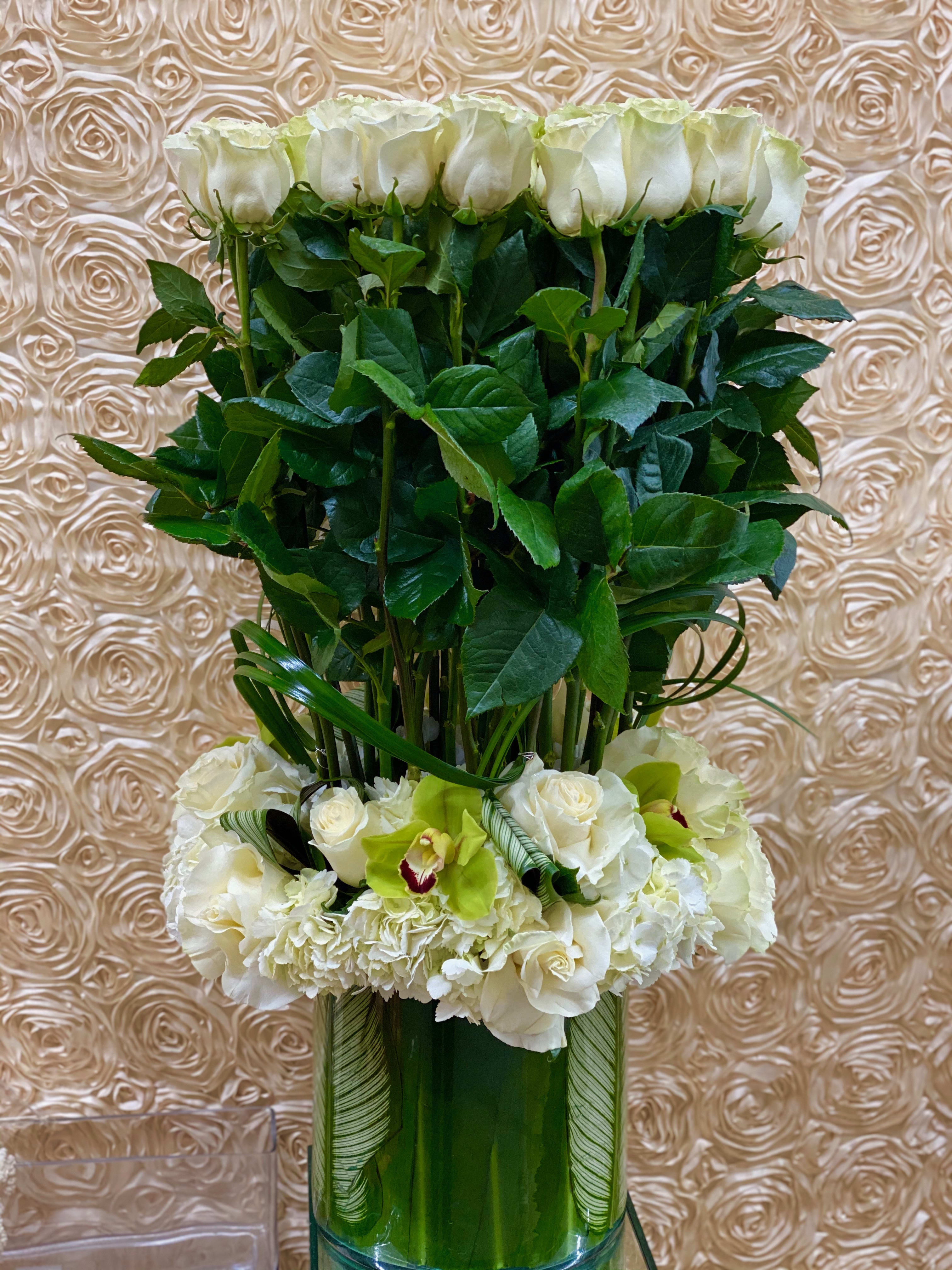 Tall white rose arrangement with orchids and hydrangeas in a glass vase