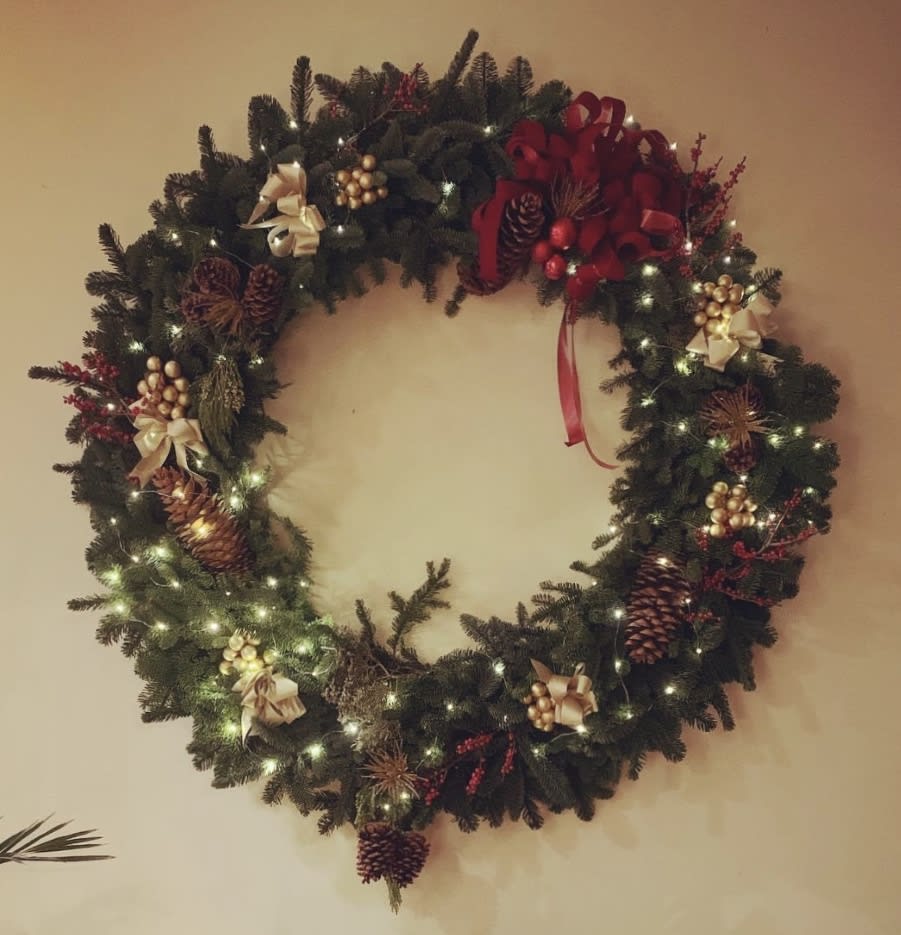 Decorated evergreen wreath with lights, pinecones, bows, and red accents
