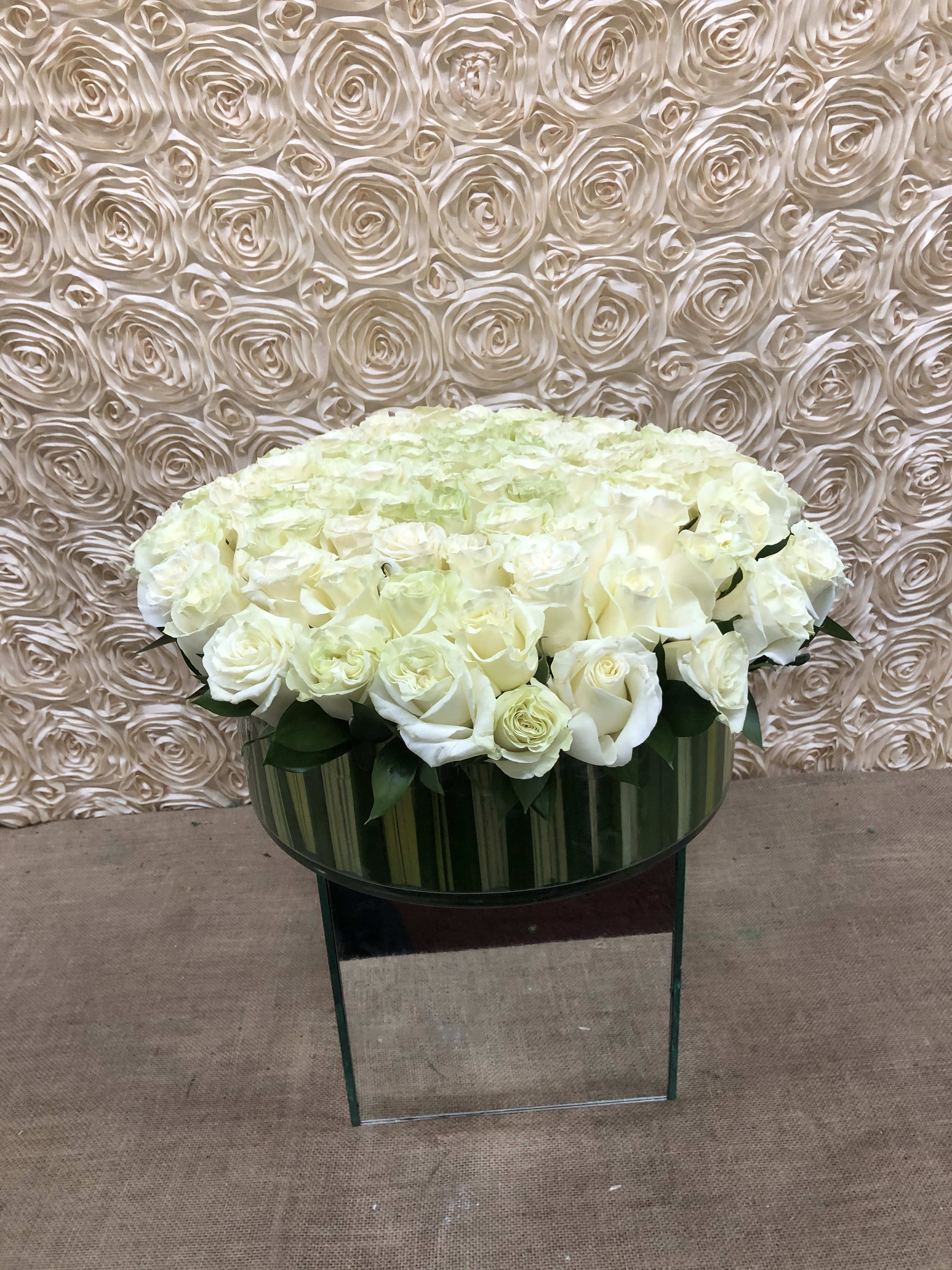 Large white rose arrangement in a glass vase on a mirrored stand