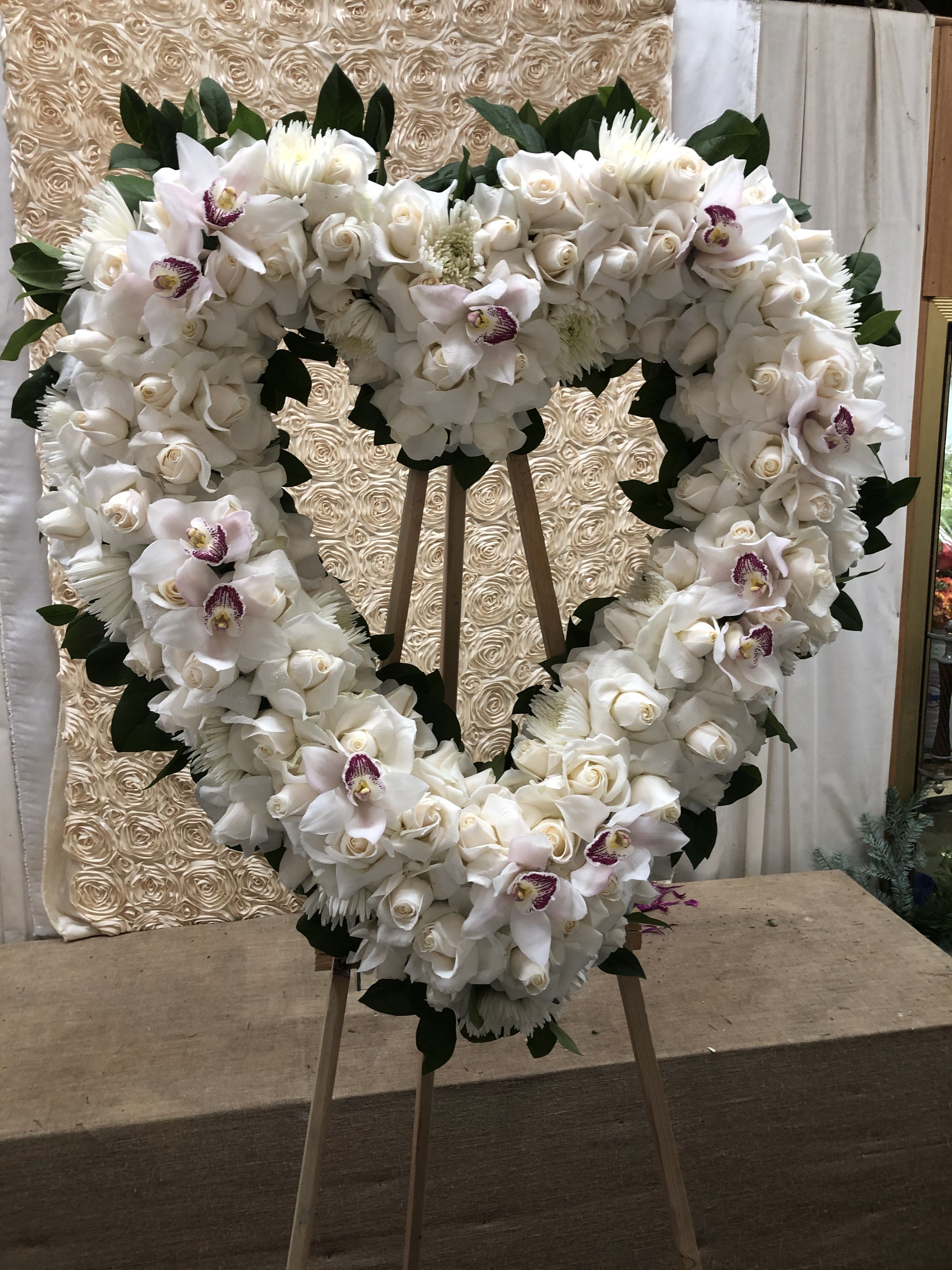 Heart-shaped white floral wreath on an easel with orchids and roses