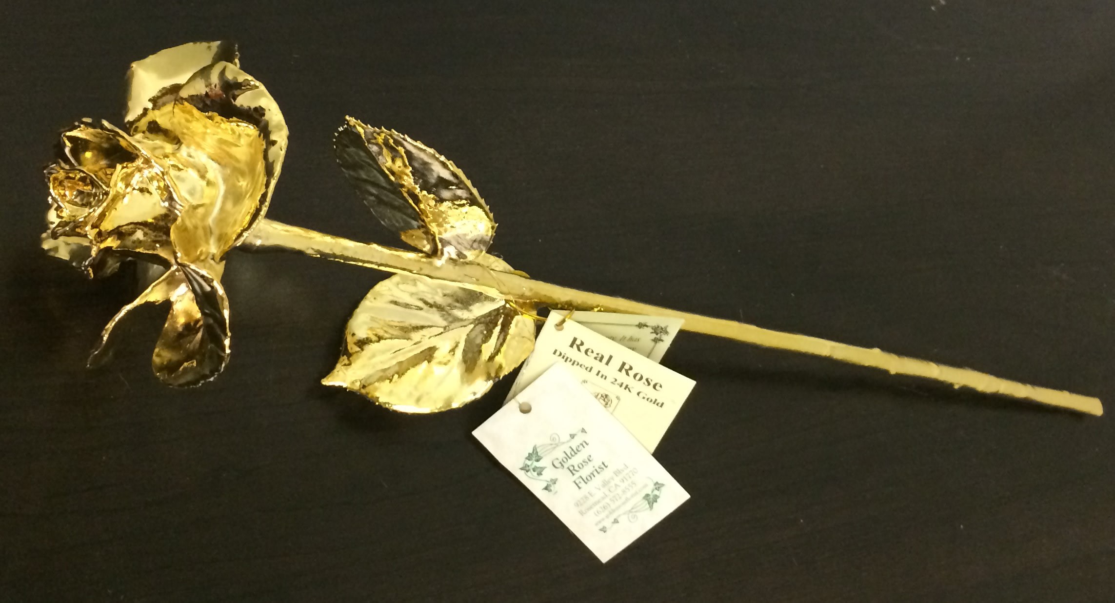 Single gold-dipped rose with attached tags on a black background