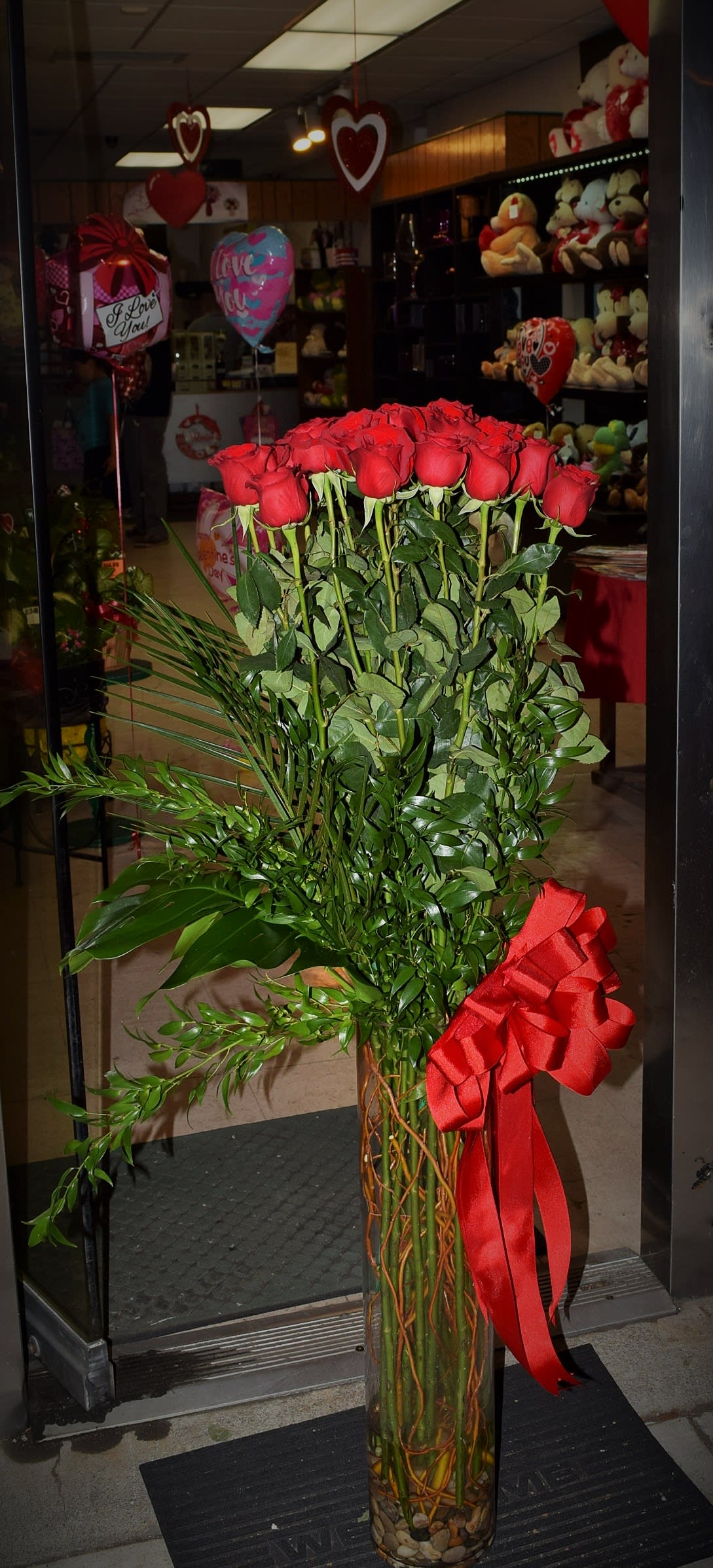 Tall bouquet of red roses in a glass vase with a red ribbon