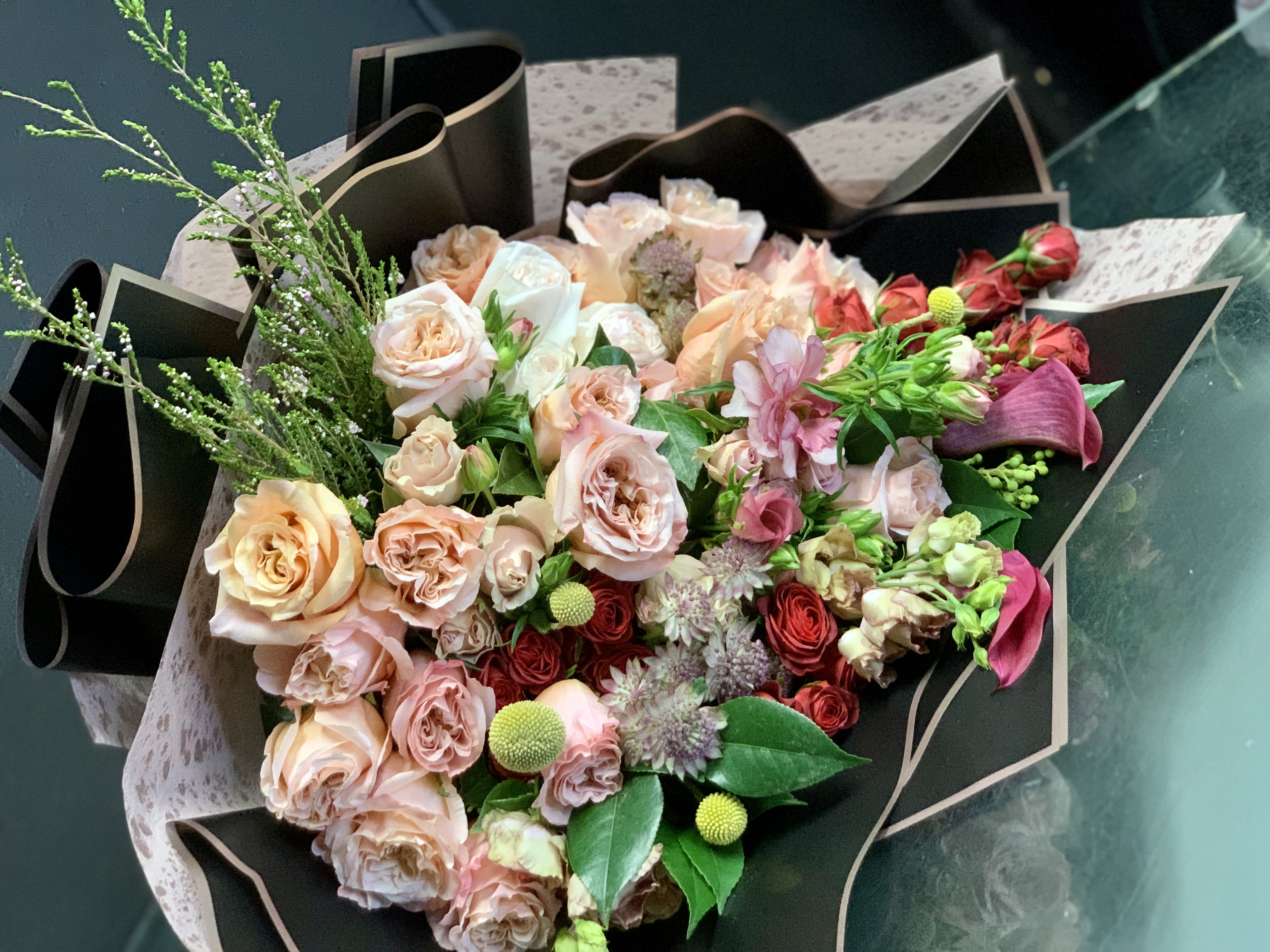 Bouquet of blush and peach roses with pink accents wrapped in black paper