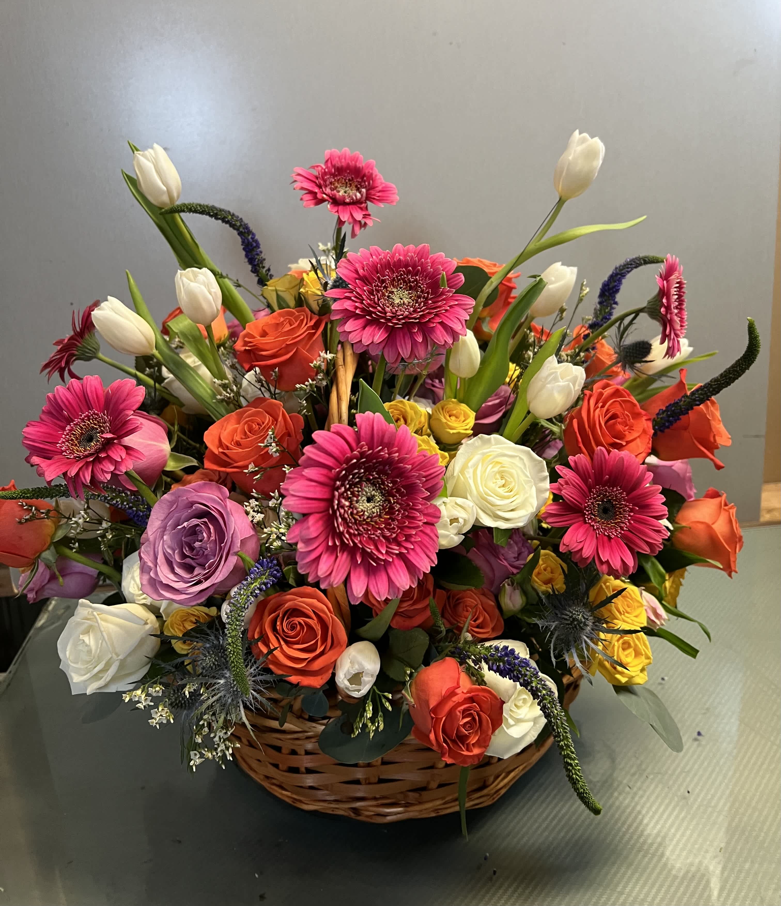 Mixed bouquet in a wicker basket with pink gerberas, roses, and white tulips