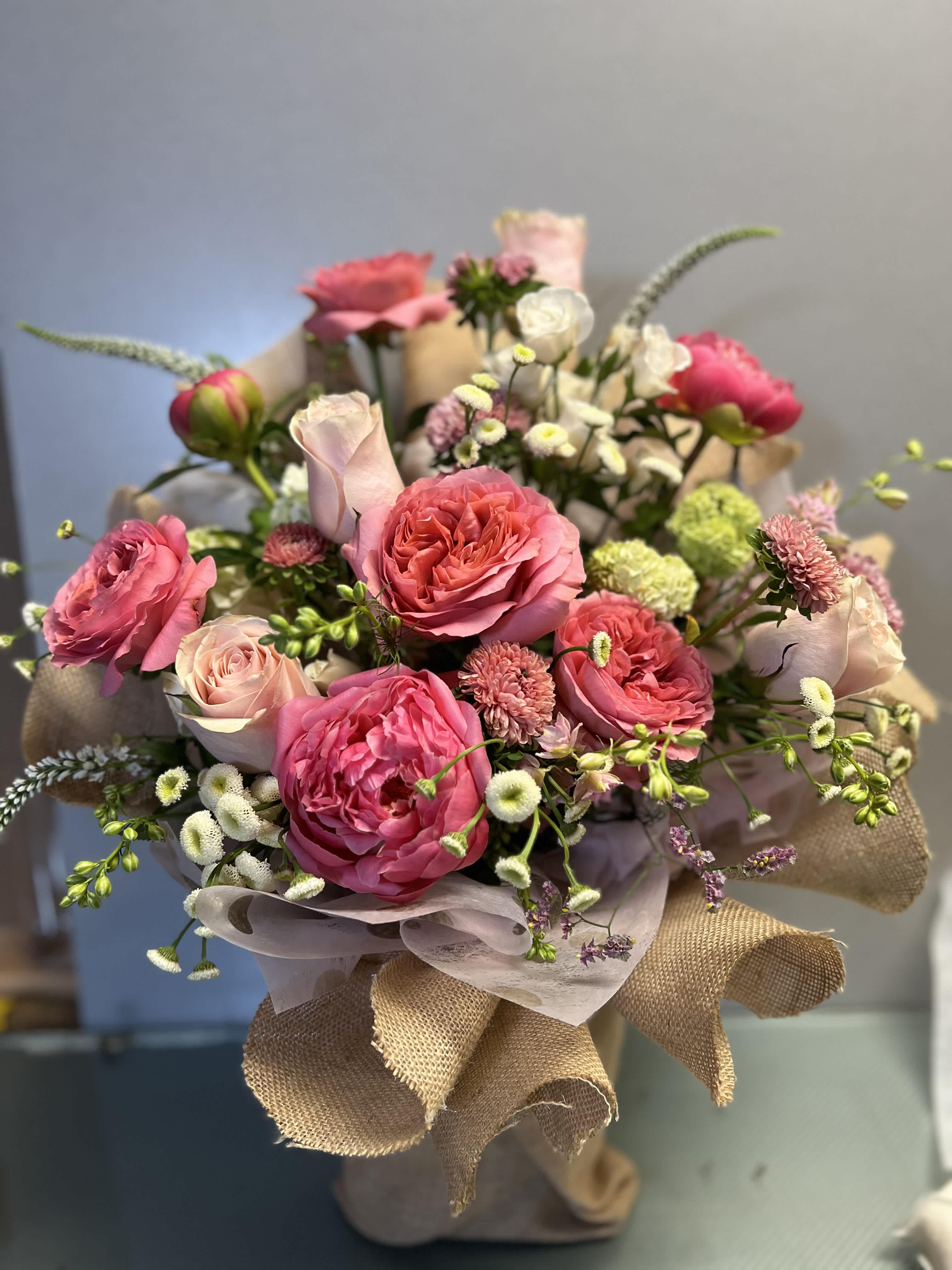 Bouquet of pink roses and small white flowers wrapped in burlap