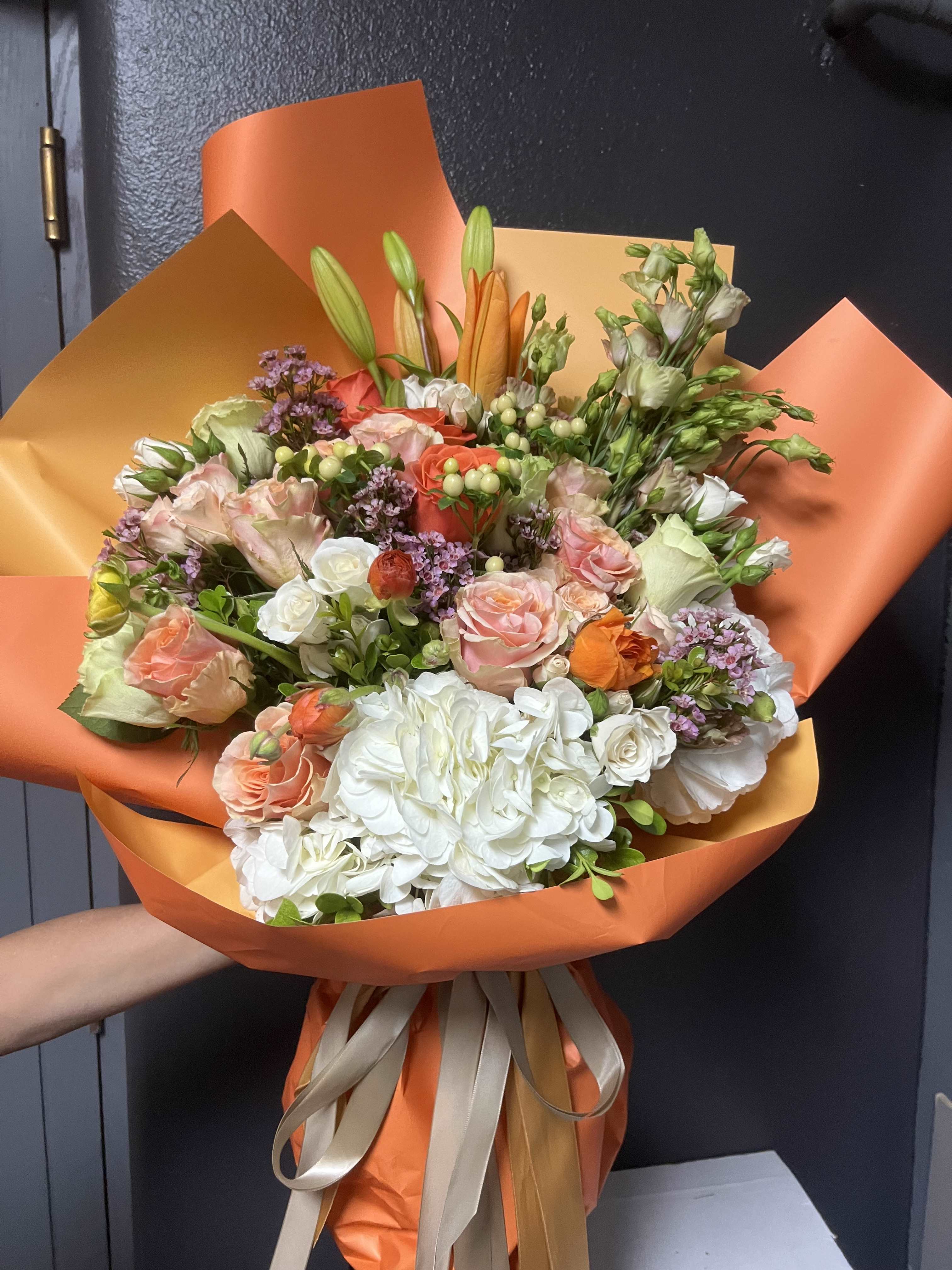 Bouquet of pink, white, and orange flowers wrapped in orange paper