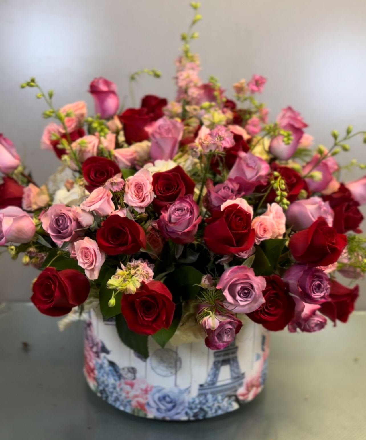 Bouquet of red, pink, and lavender roses in a decorative round box
