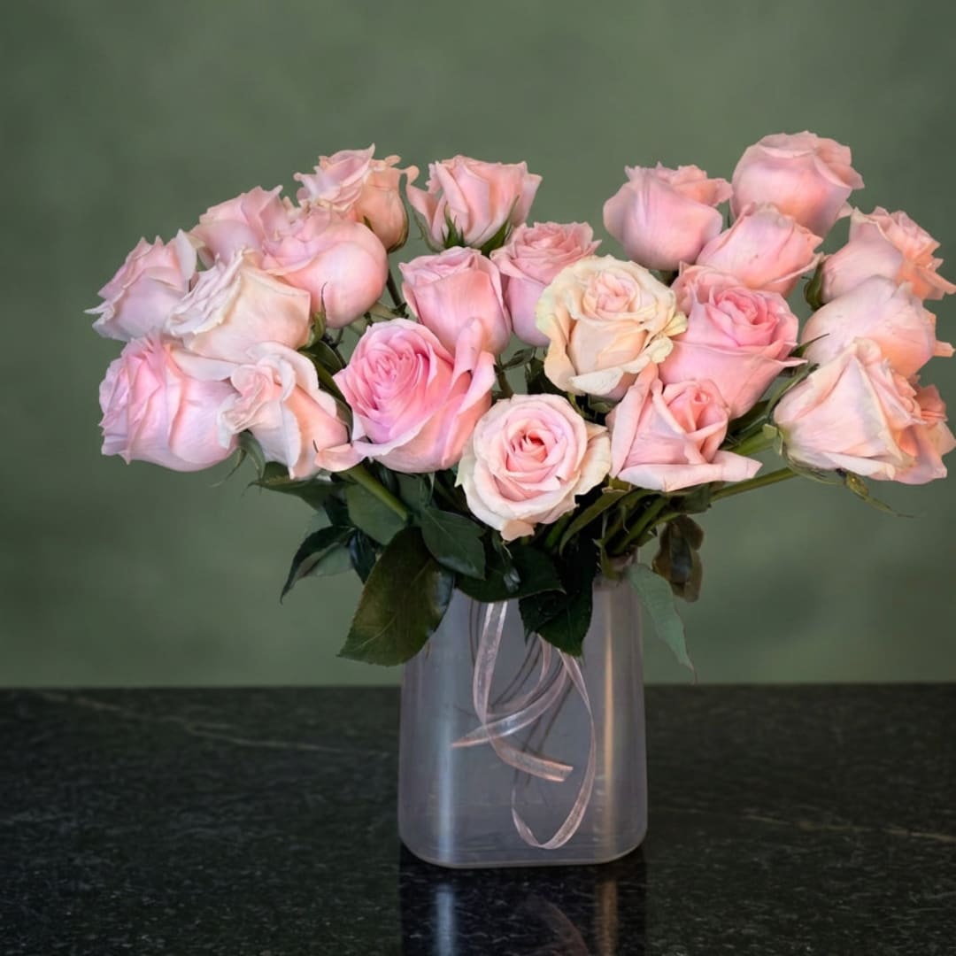 Pink roses arranged in a clear square vase with a ribbon