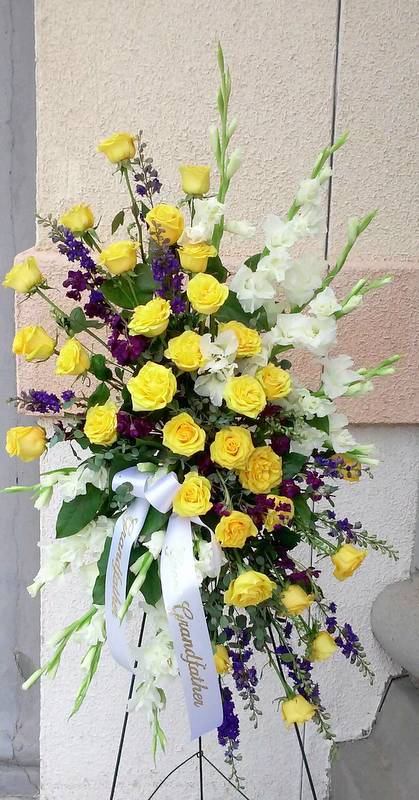 Tall standing spray of yellow roses, white gladiolus, and purple accents