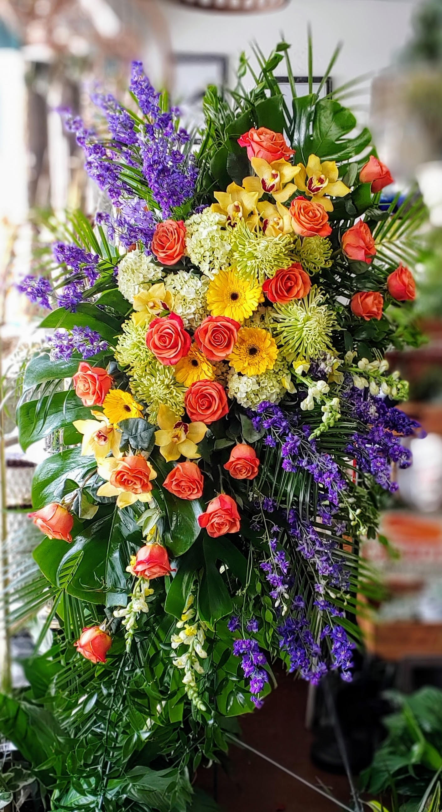 Large standing floral spray with orange roses, yellow orchids, and purple blooms