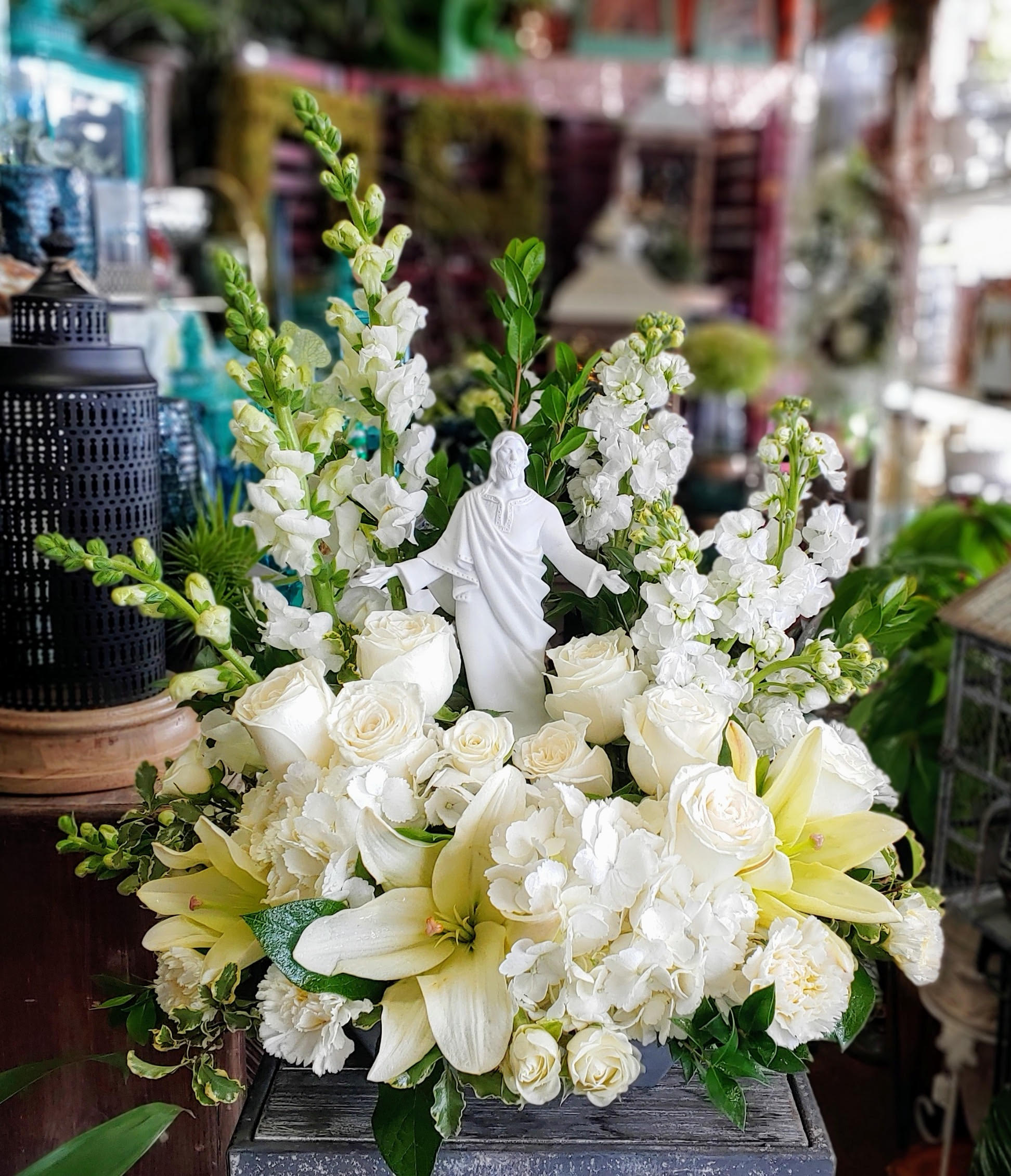 White floral arrangement with roses, lilies, and a small statue centerpiece