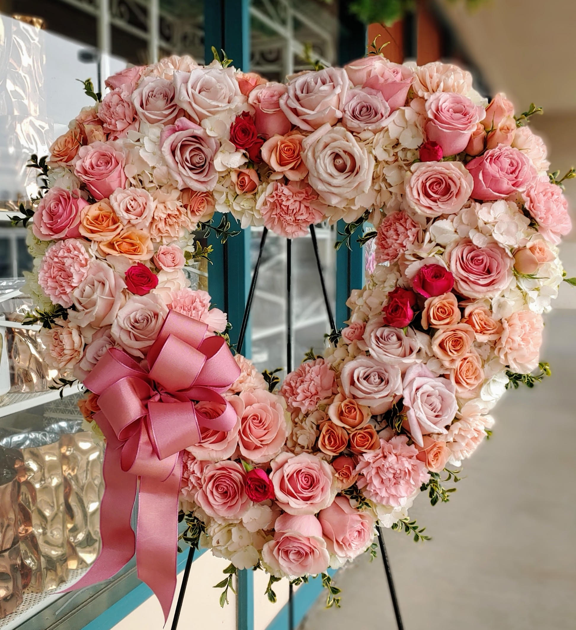 Heart-shaped pink and peach rose arrangement with a satin bow