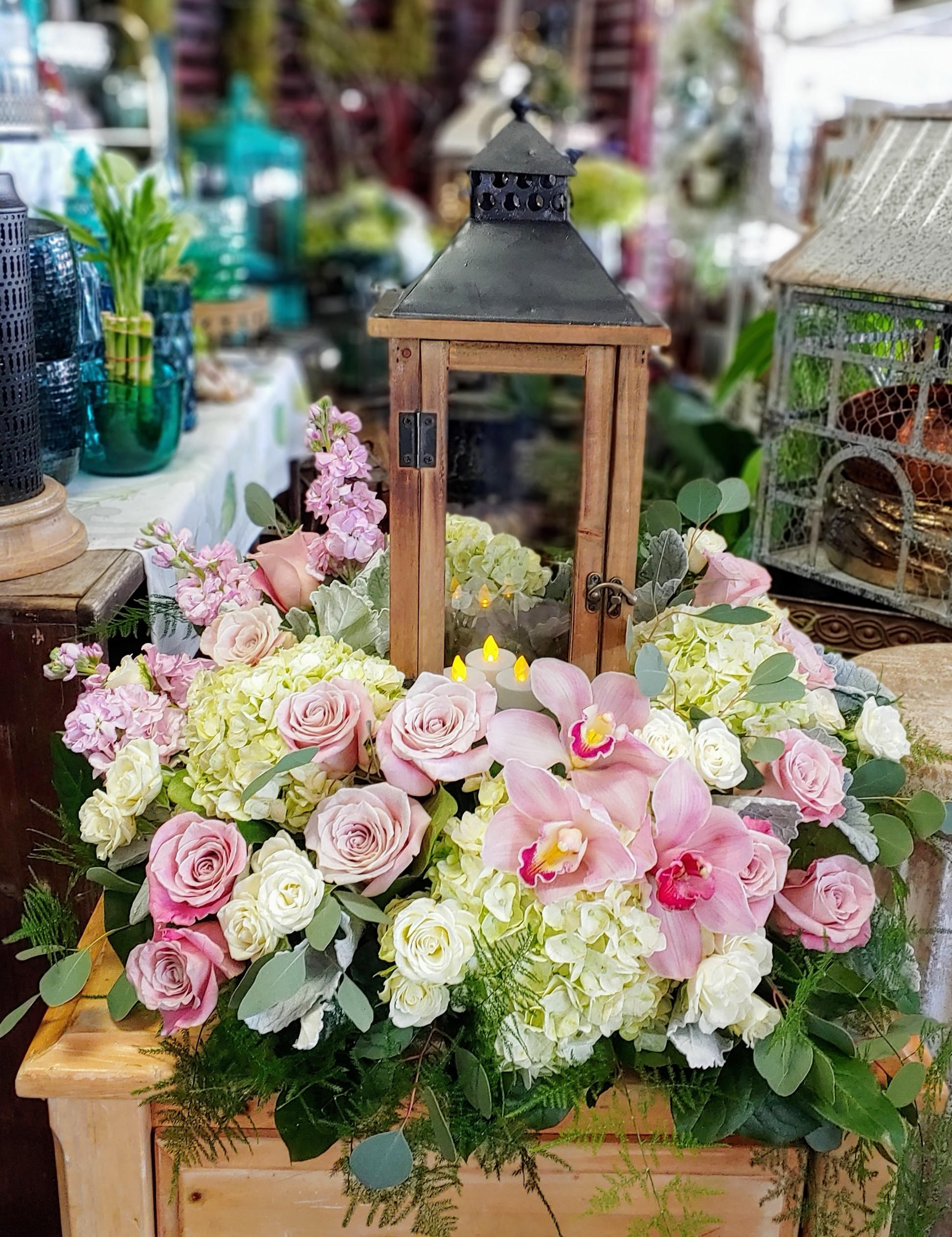 Pink roses and orchids arranged around a wooden lantern centerpiece