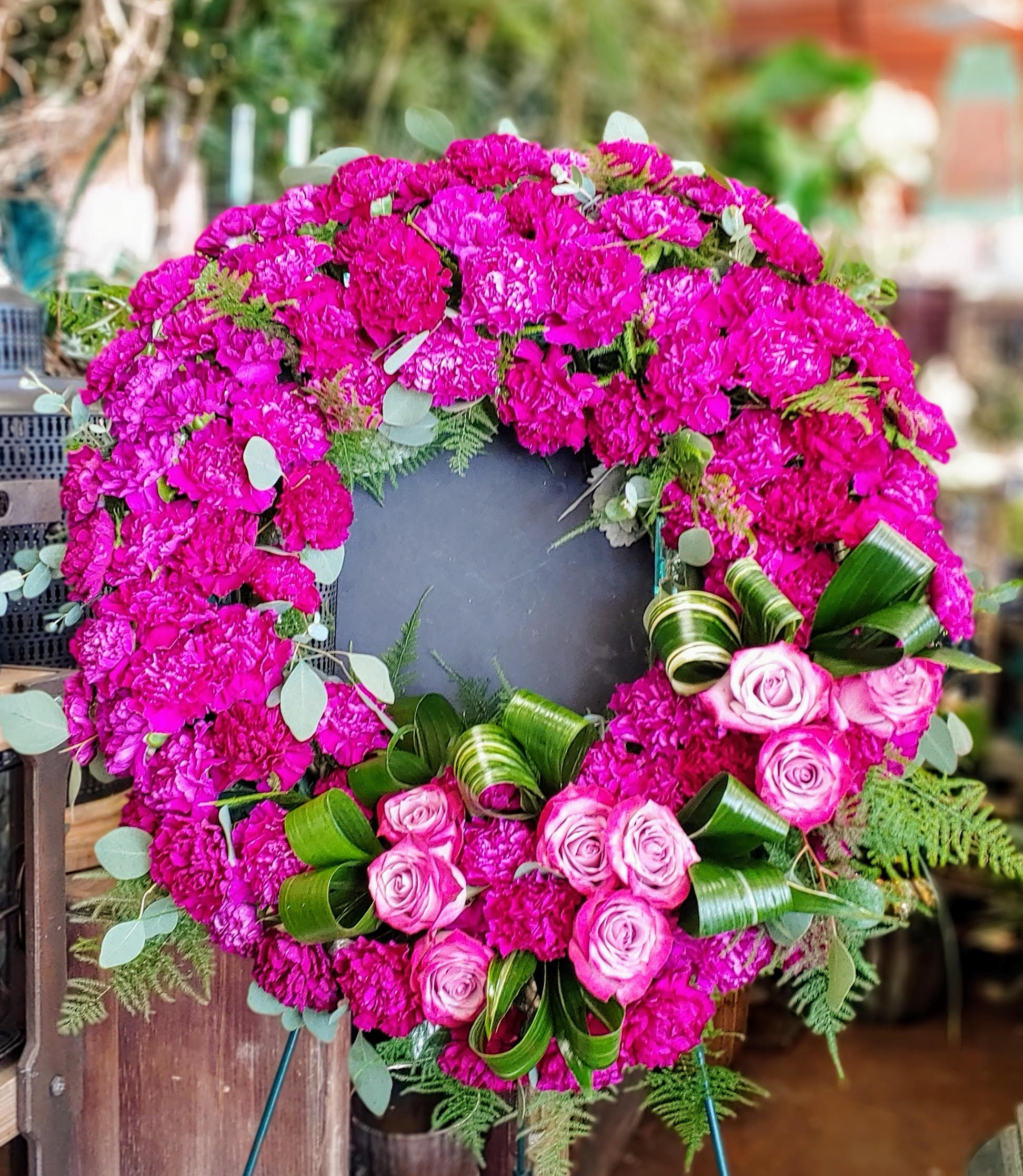 Radiant Remembrance - Vivid and full of love, Radiant Remembrance is a striking floral wreath that honors life with bold beauty and heartfelt color. Deep magenta carnations form a lush, velvety ring—each petal rich with texture and intensity—while Lavender and fuchsia roses gather at the base like whispers of grace and affection. Elegant loops of variegated aspidistra leaves add structure and flow, weaving through the blooms with modern sophistication.  Hints of eucalyptus and feathery ferns peek out, offering a touch of greenery and freshness to this vibrant tribute. Whether displayed at a memorial, celebration of life, or farewell service, this wreath speaks volumes of the light someone brought into the world.  Handcrafted with care by Windmill Floral Expressions in Las Vegas. Available for delivery in Las Vegas and Henderson.