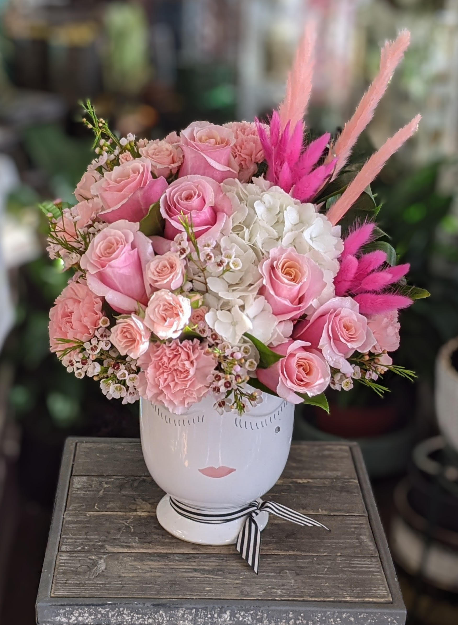 Pink roses and white hydrangeas in a white face vase with pink feathers