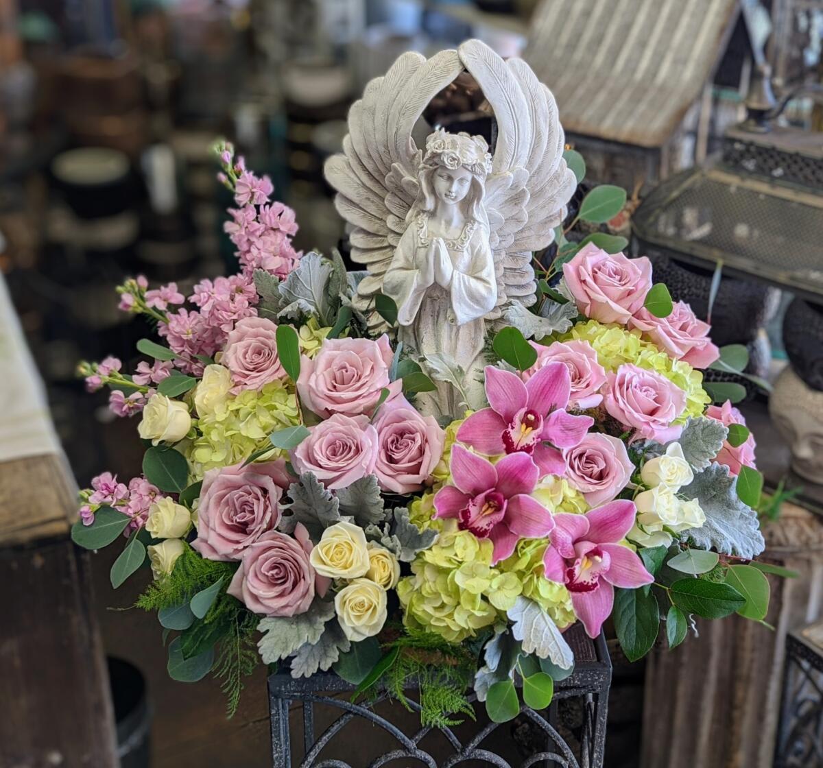 Pink roses and orchids arranged around a white angel statue
