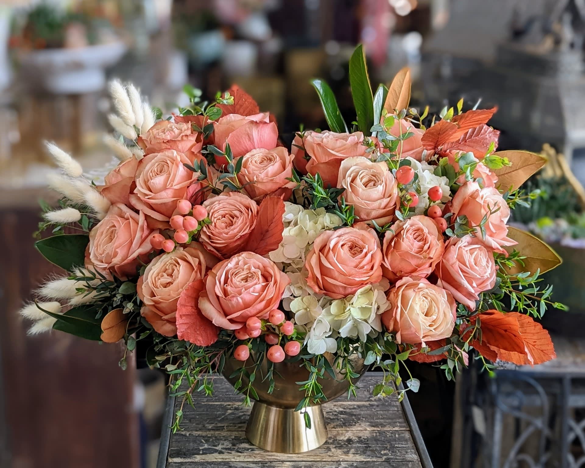 Peach rose arrangement in a gold vase with white accents and autumn foliage