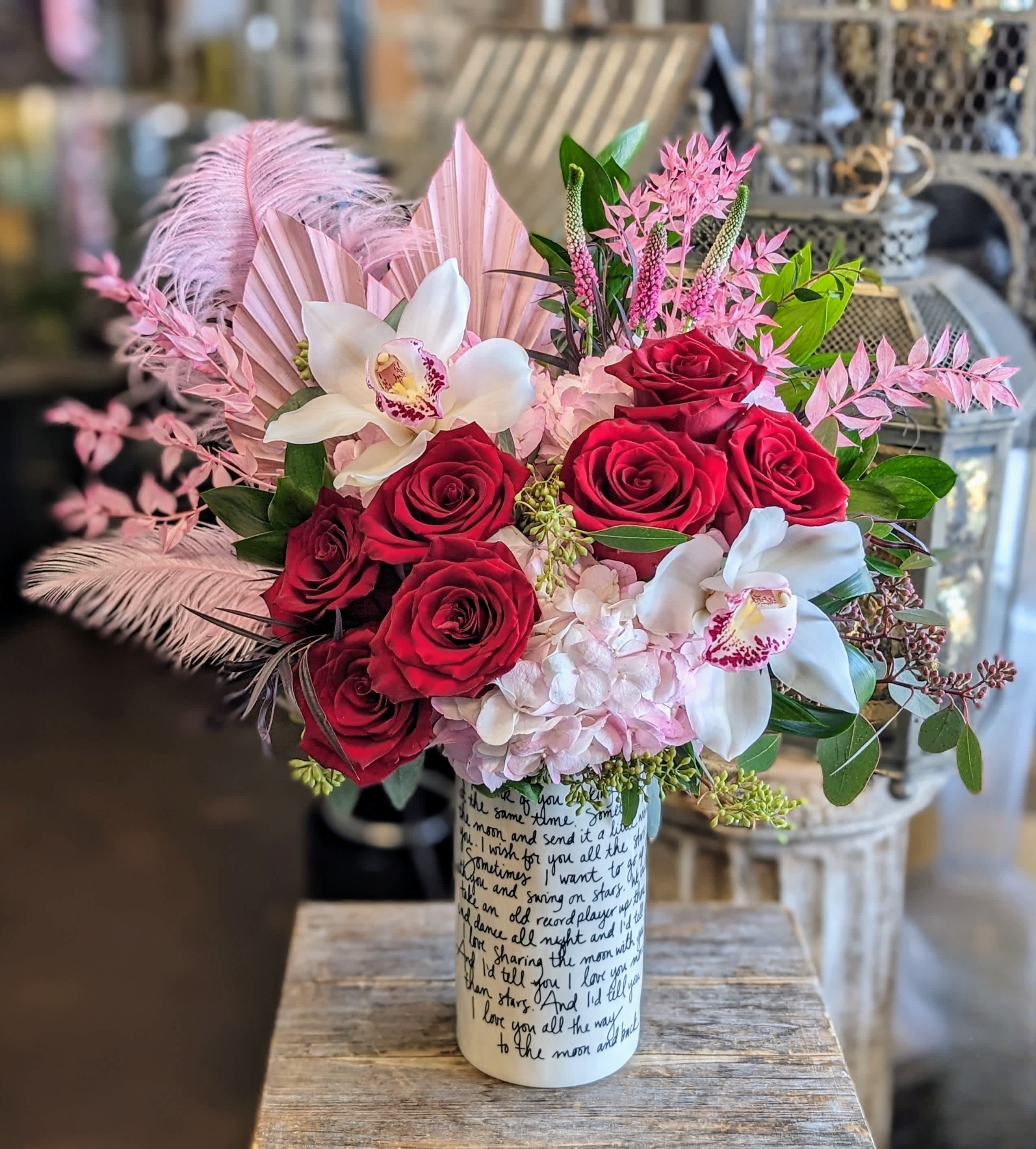 Bouquet of red roses and white orchids in a printed vase with pink feathers