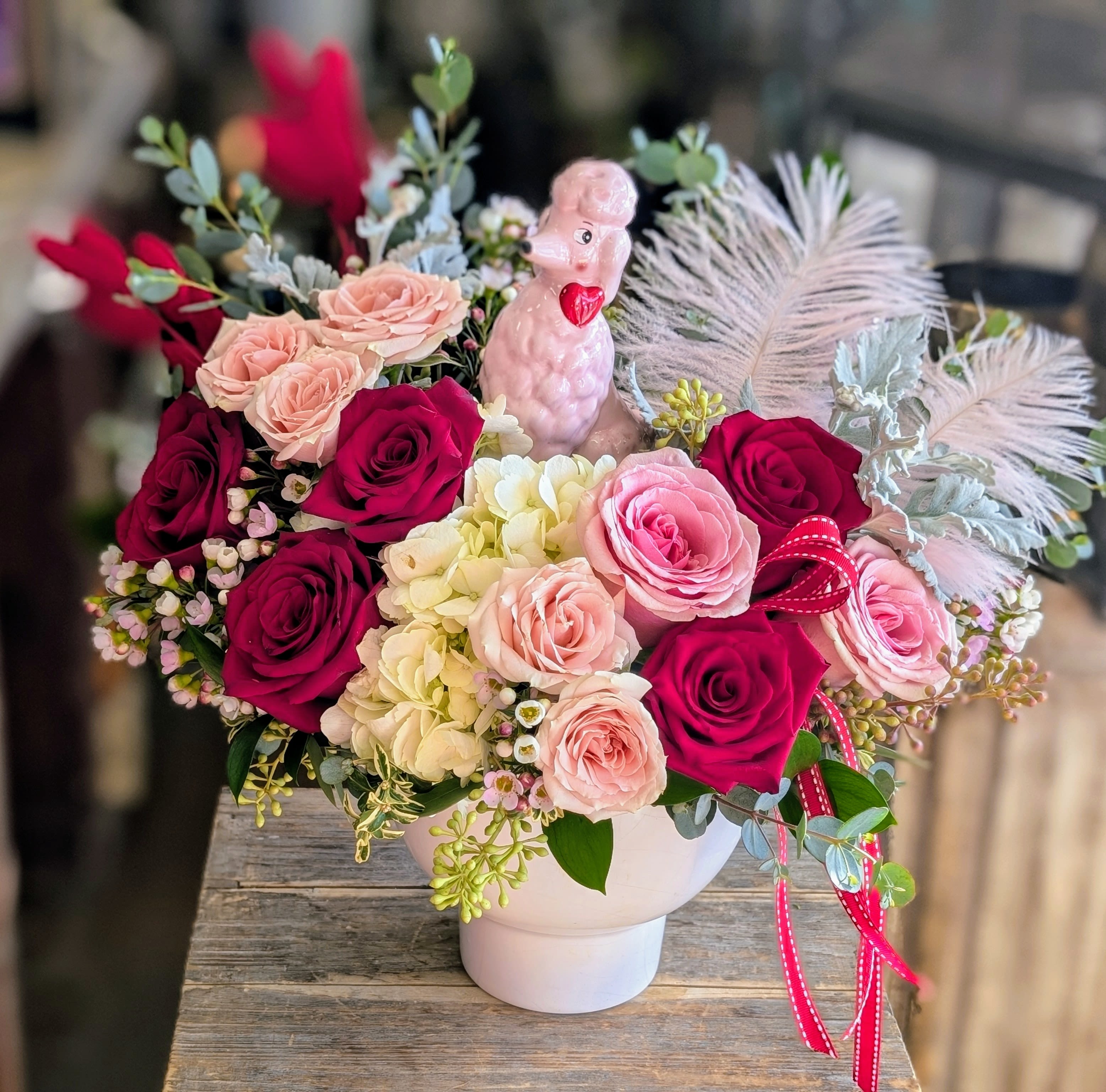 Pink and red rose arrangement in a white vase with a small poodle figurine