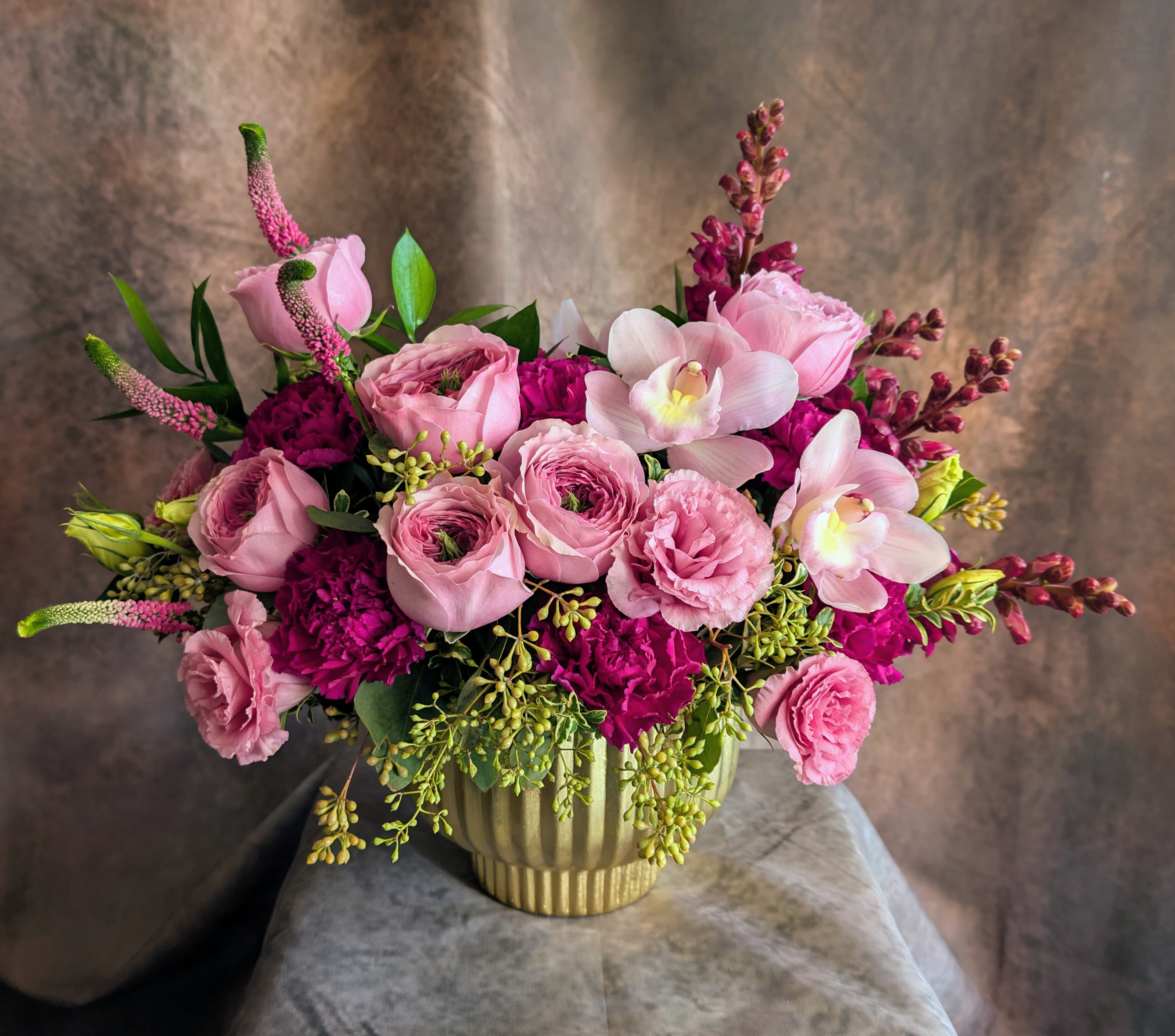 Maeve - Maeve is our pink-and-plum beauty—romantic, moody, and effortlessly feminine. Designed by Windmill Floral Expressions in Las Vegas, this arrangement showcases lush Peonikiss roses, soft lisianthus, blush cymbidium orchids, and rich plum blooms that add depth, contrast, and a little bit of drama.  Nestled in a chic gold vessel, Maeve blends airy pink textures with saturated plum tones, creating a striking, vintage-inspired look that feels both modern and timeless. Perfect for birthdays, anniversaries, thoughtful surprises, or anyone who loves that pink-but-make-it-bold vibe.  Hand-crafted with premium blooms and delivered with care across Las Vegas, Henderson, Anthem, Inspirada, Seven Hills, and MacDonald Ranch, Maeve brings a touch of floral luxury to every space. Same-day delivery available. Custom designs always welcomed.