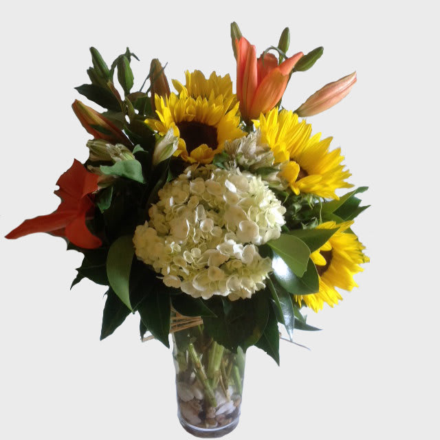 Brightly  - Flowers Included: White Hydrangeas: 3 Stork flowers: 3 Lilies: 3 Sunflowers: 5  Also Included:  Glass Vase &amp; Greenery