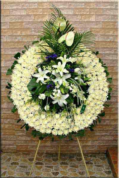 Large standing floral wreath with white lilies and pale blooms on an easel