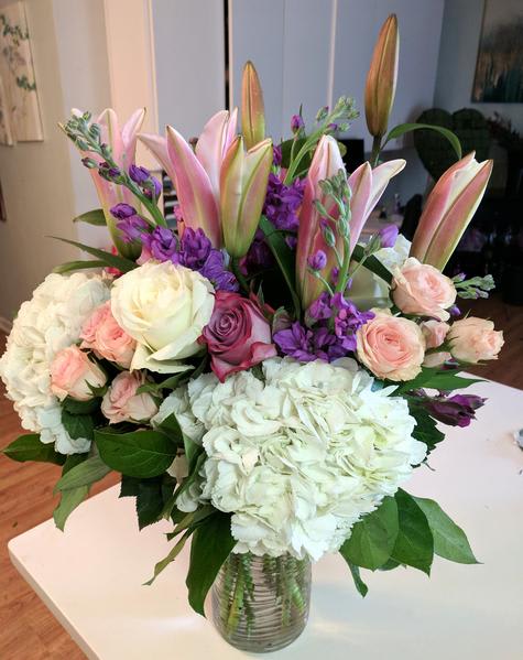 Bouquet of pink lilies, roses, hydrangeas, and purple flowers in a glass vase