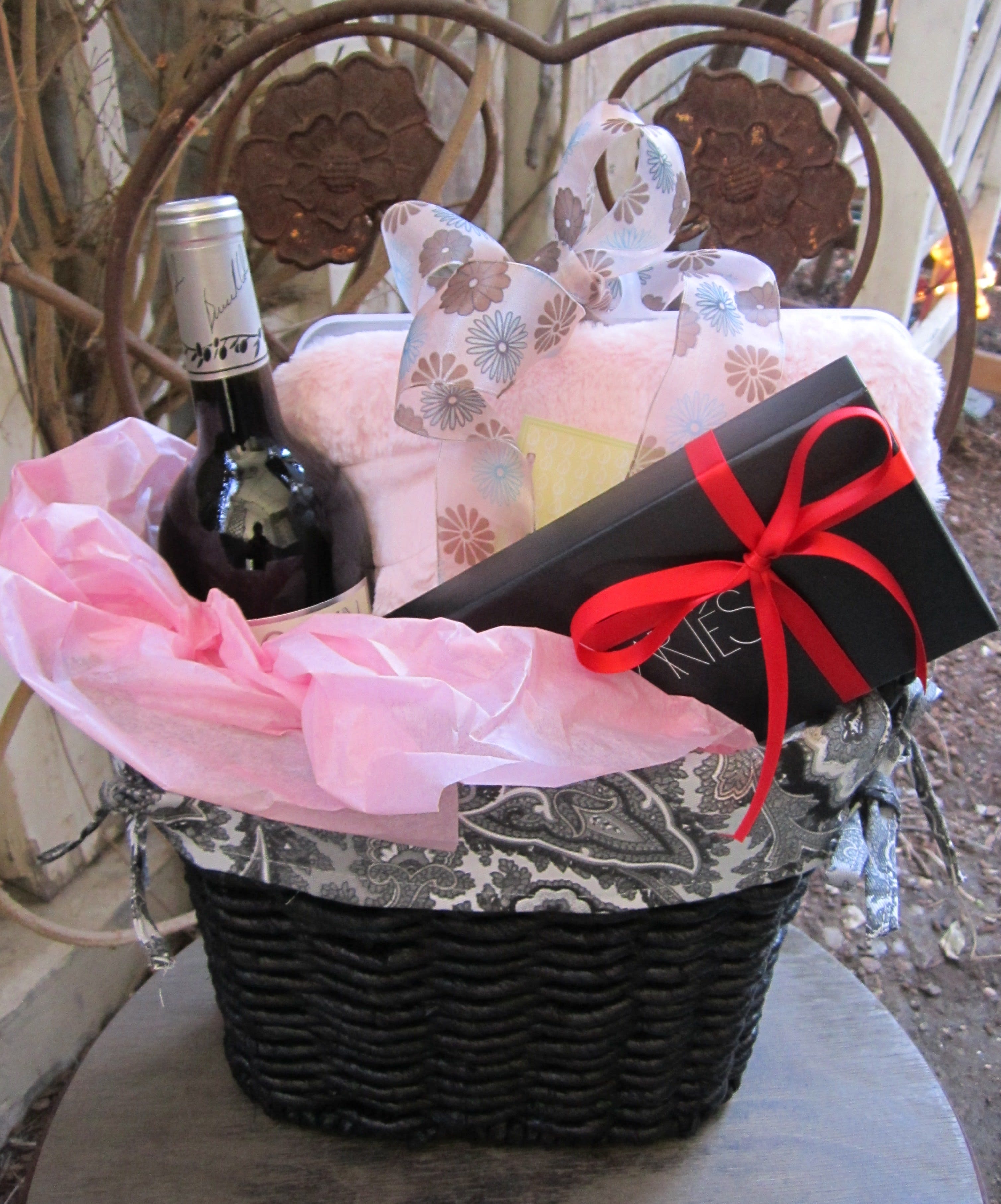 Gift basket with a wine bottle, wrapped box, and black gift box with red ribbon