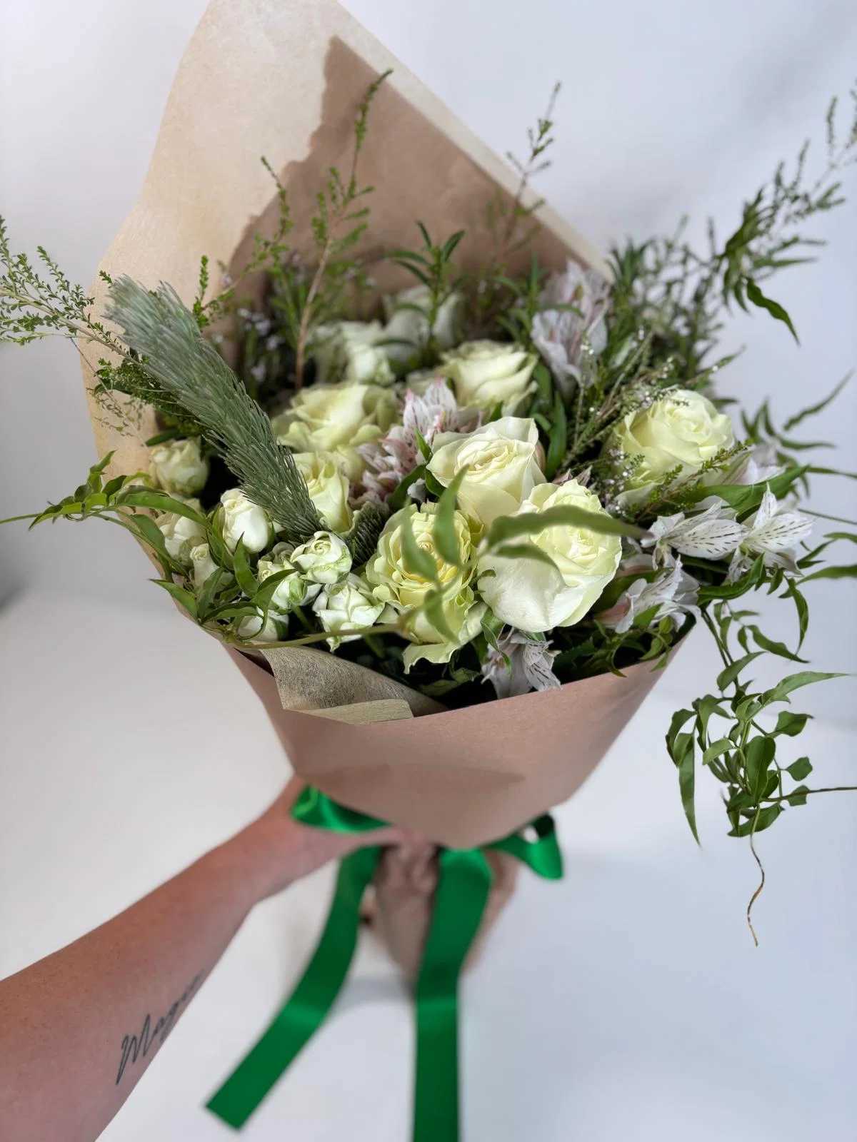 Bouquet of white roses with greenery wrapped in brown paper and tied with a green ribbon